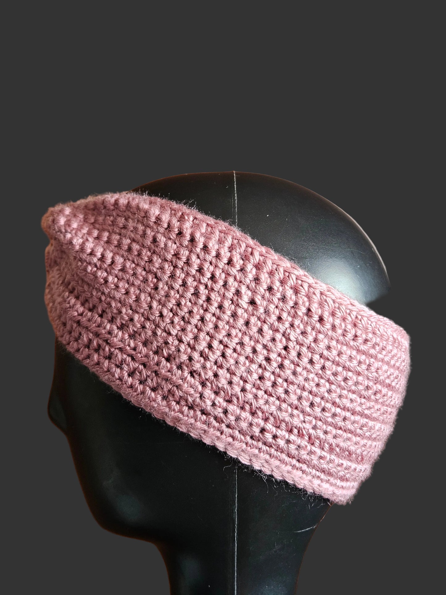 Pink knitted headband on a black mannequin head against a wooden background